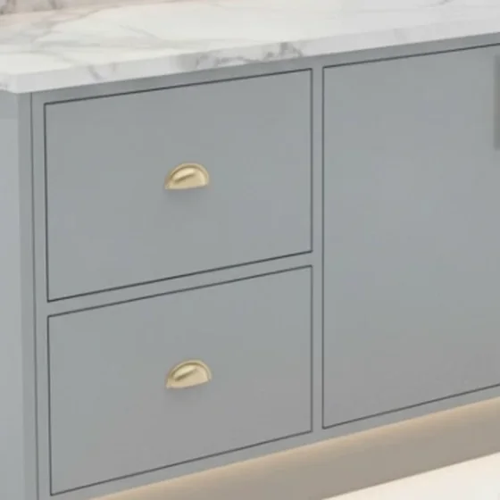 Close-up of a solid brass cup pull on a grey drawer.