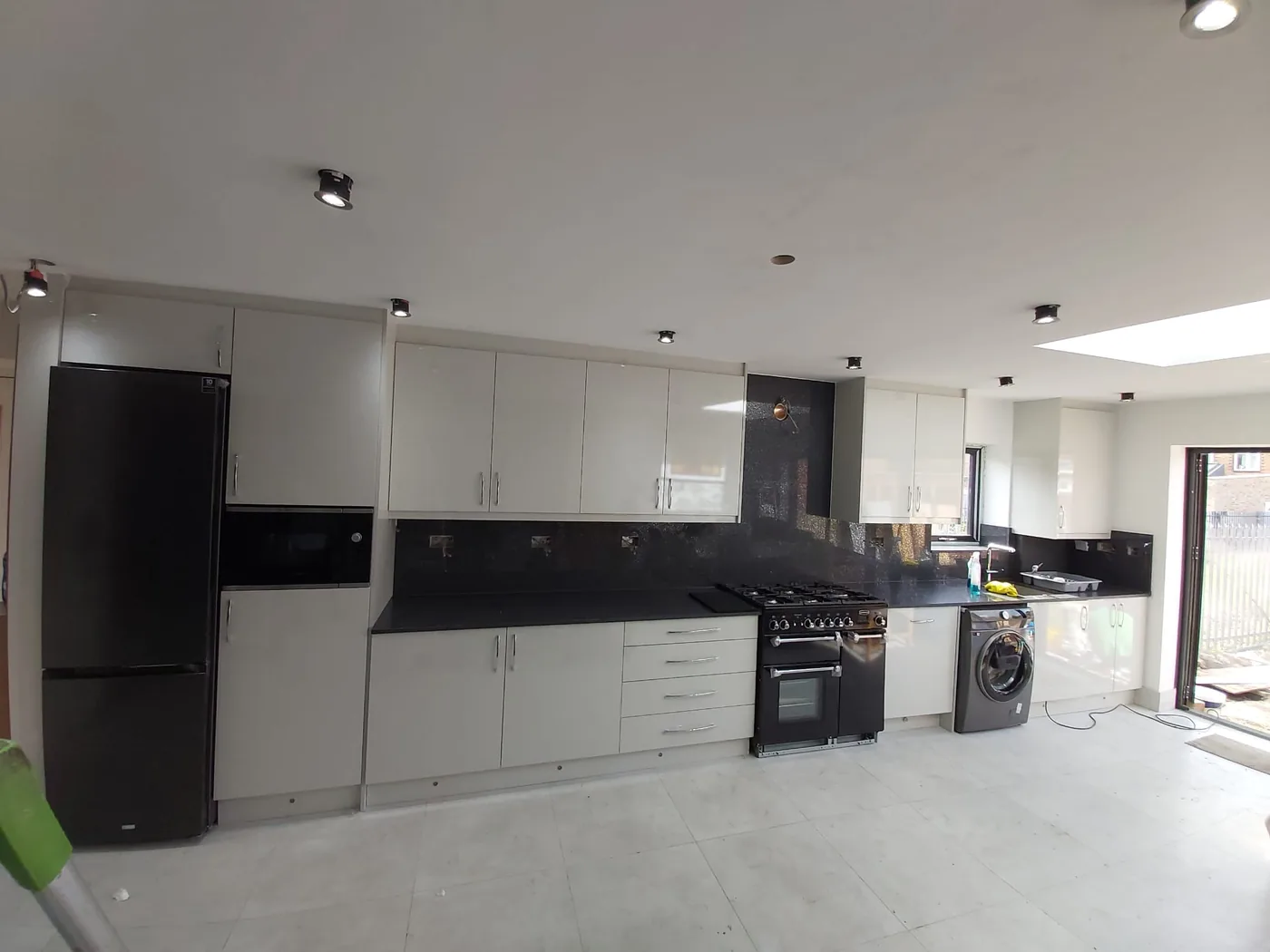 Cream gloss galley kitchen · black splashback · integrated appliances