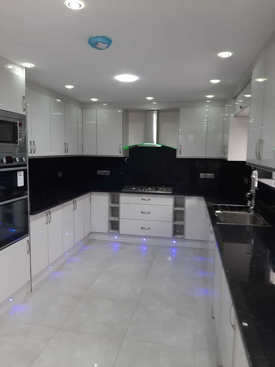 White gloss U-shape kitchen · black sparkle worktop · LED plinth lighting