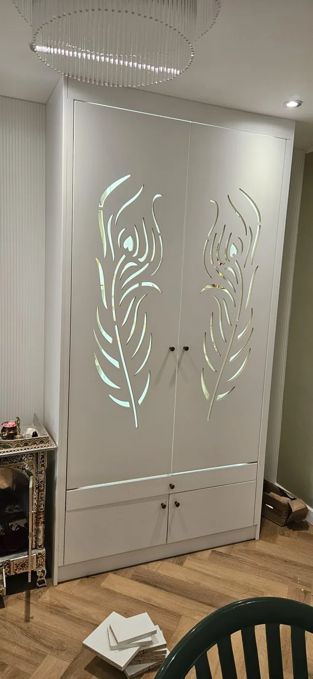 White wardrobe-style mandir · laser-cut peacock feather doors