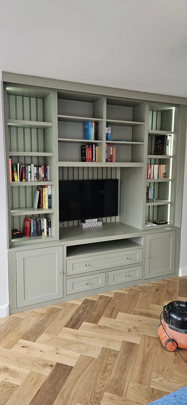 Sage full-wall TV & bookshelf unit · herringbone floor
