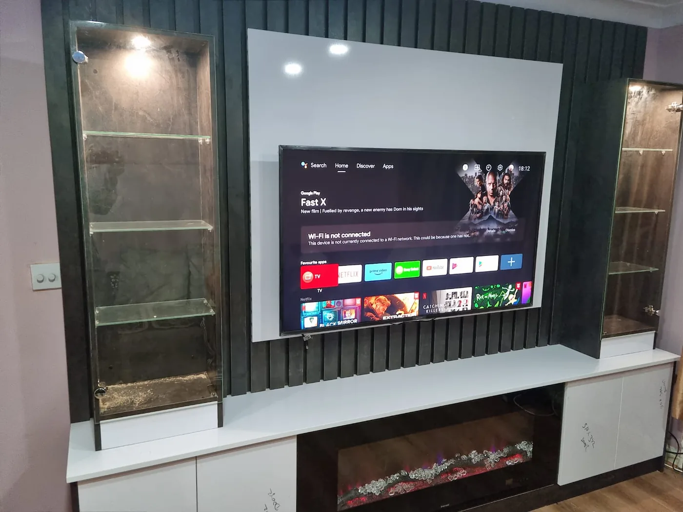Charcoal slatted media wall · twin glass display towers · built-in fire