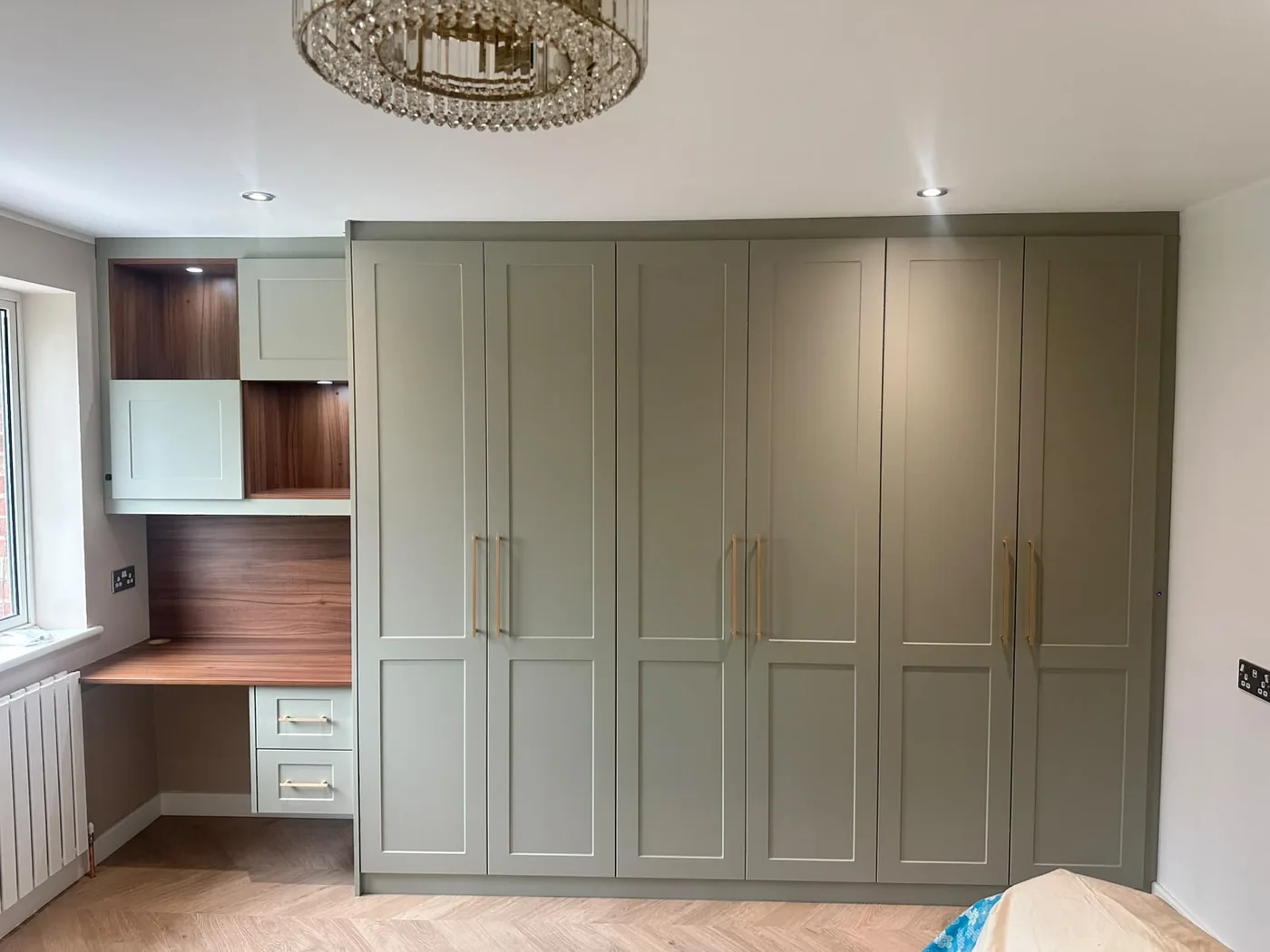 Sage green fitted wardrobe · walnut desk nook · chandelier